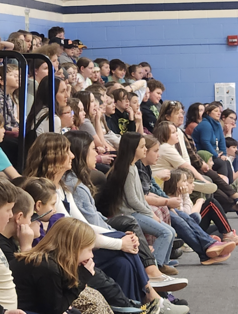 Close view of older elementary and middle school students seated closely together on bleachers, attentively watching a school assembly.