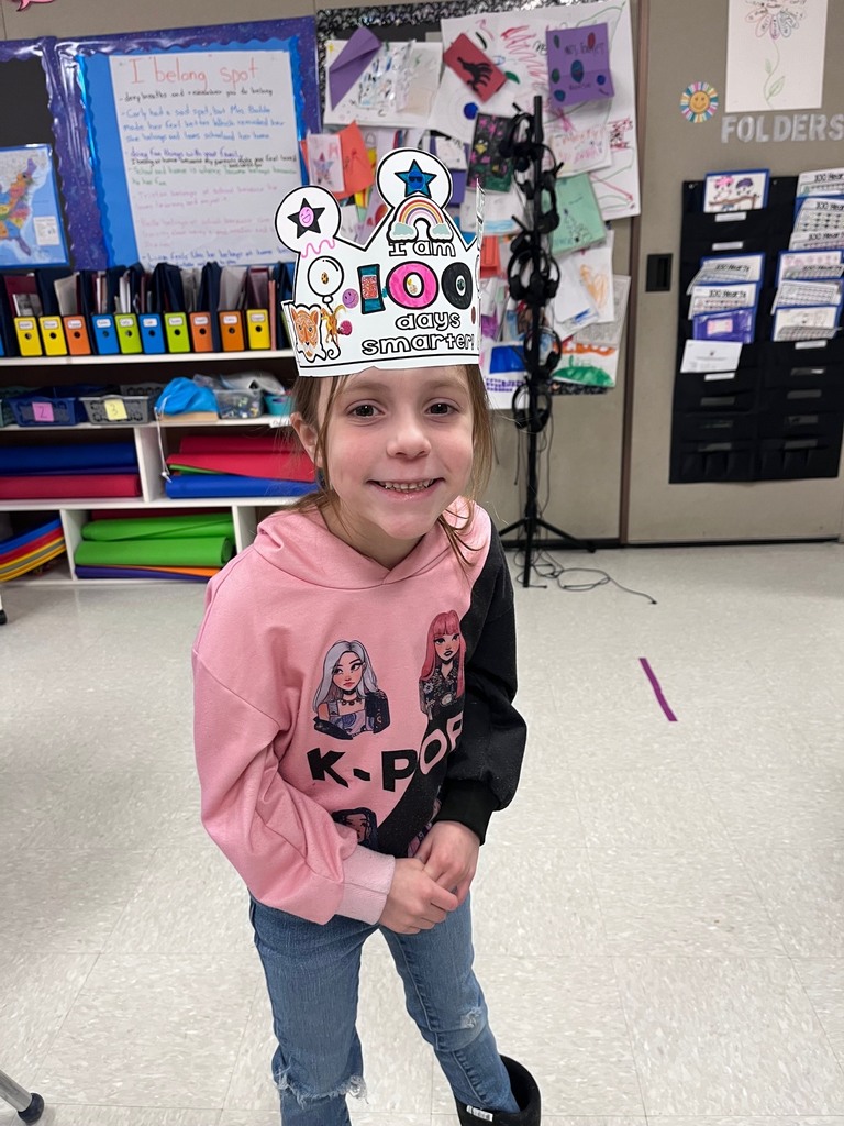 A girl wearing a pink and black color-blocked "K-POP" hoodie posing in a classroom. Her crown is white with a rainbow sticker in the center.