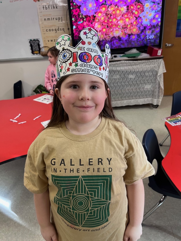 A girl in a tan "Gallery in the Field" t-shirt wearing a crown decorated with many small star stickers and a large eye sticker on the side.
