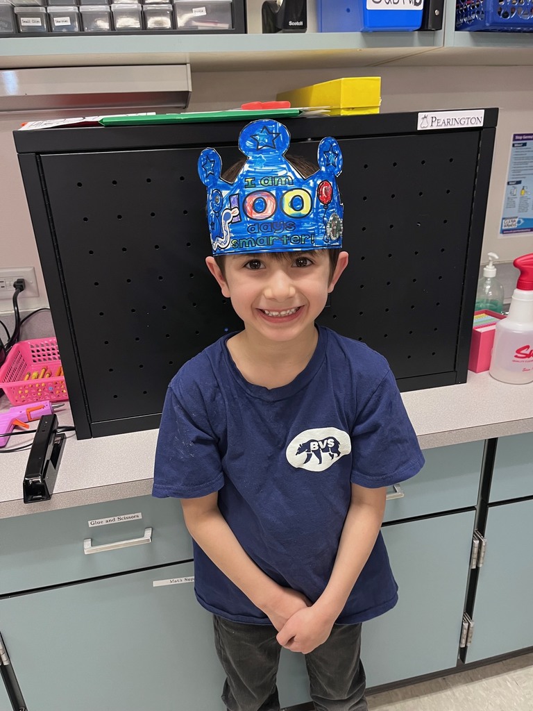  A young boy in a navy blue t-shirt beams at the camera. He has colored his entire crown with a vibrant blue marker, leaving the "100" and the "I am... smarter!" text visible through the ink. 