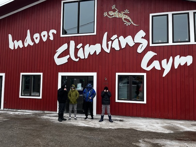 Group of students standing outside a red building labeled “Indoor Climbing Gym” on a winter day.