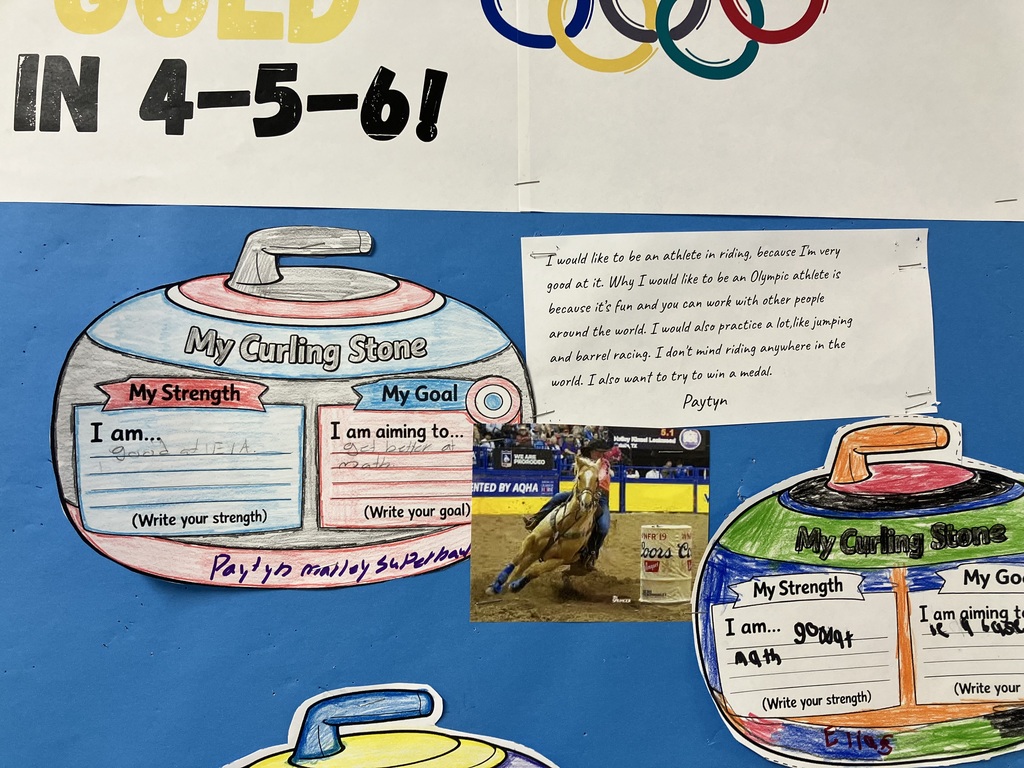 Bulletin Board Overview Context: A blue bulletin board features a large banner at the top with the Olympic rings and the text "GOING FOR GOLD IN 4-5-6!"  Layout: Below the banner are several hand-colored paper cutouts shaped like curling stones. Each stone is divided into two sections: "My Strength" and "My Goal."  Details: One stone by a student named Paytyn lists a strength in "ELA" and a goal to "get better at math." Next to it is a printed essay and a small photograph of a person competing in barrel racing on a horse