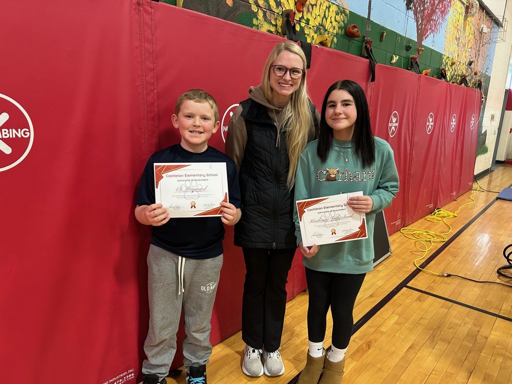 Two students holding Castleton Elementary School certificates stand with a staff member in front of red gym wall padding; all are smiling at the camera.