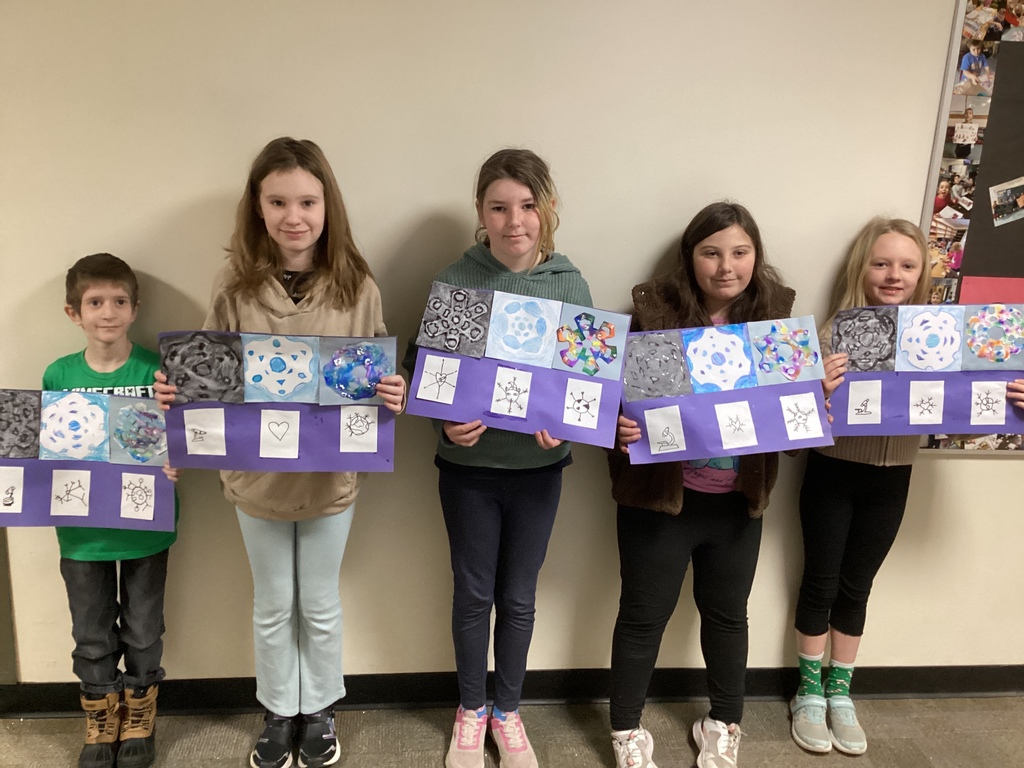 Five elementary students stand side by side against a wall, each holding a purple display board with multiple snowflake-style artworks and small black-and-white drawing studies.