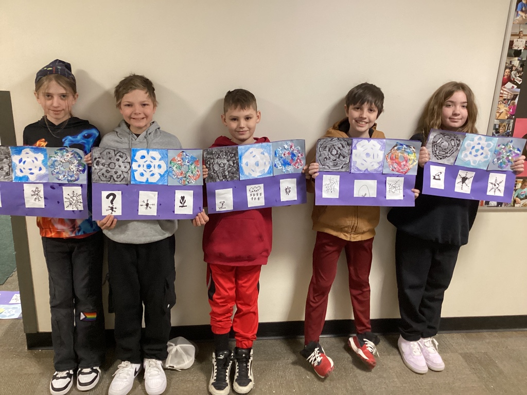Five elementary students stand in a hallway holding purple-backed art projects featuring snowflake-themed designs and small sketch panels beneath each design.