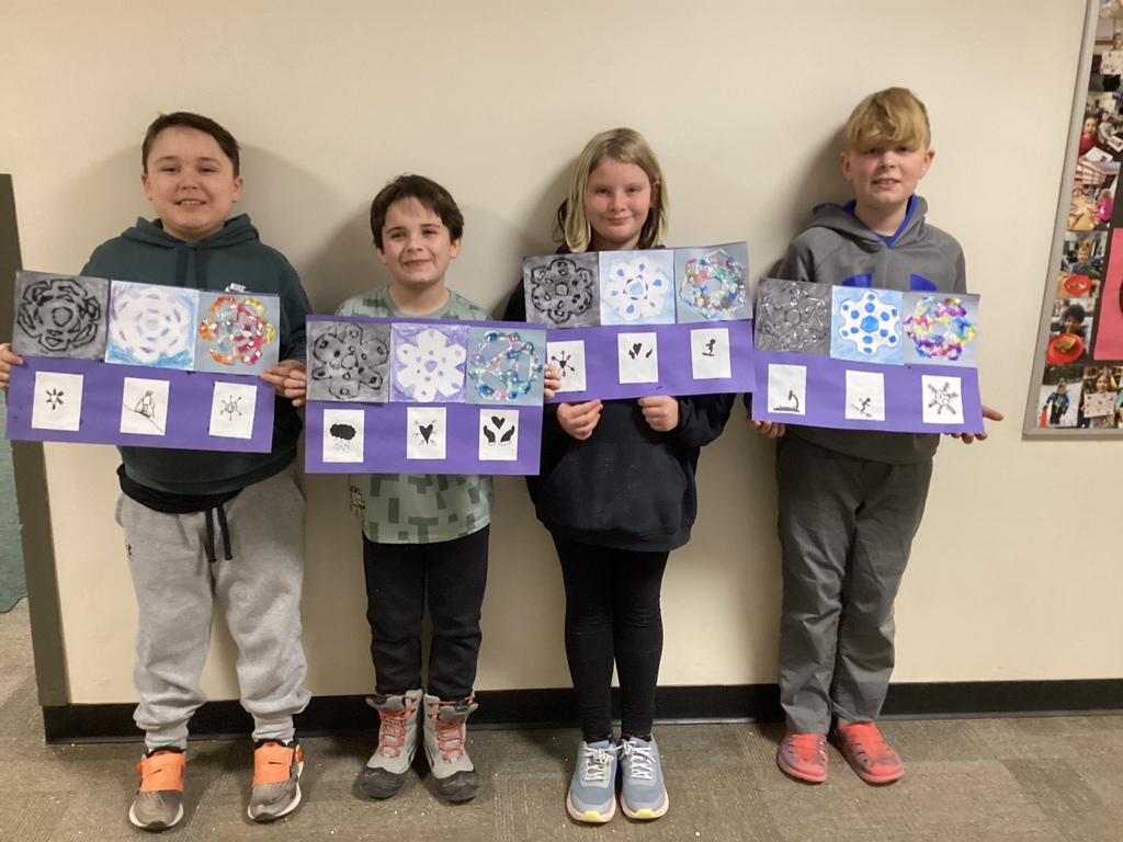 Four elementary students stand shoulder to shoulder holding purple-mounted snowflake artwork panels that include painted patterns and small observational drawings.