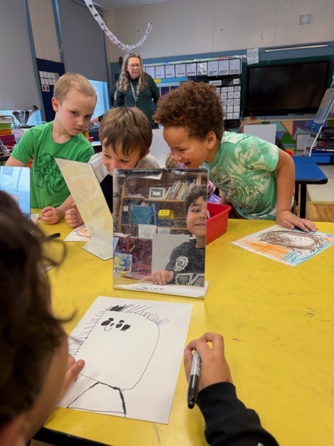 Three students lean in and smile while checking their reflections in mirrors and adding features to their portrait drawings.