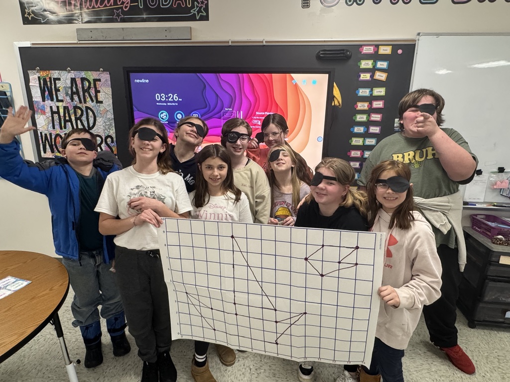 Gemini said A group of school children wearing black eye patches and holding a large graph paper drawing of a boat in a classroom.