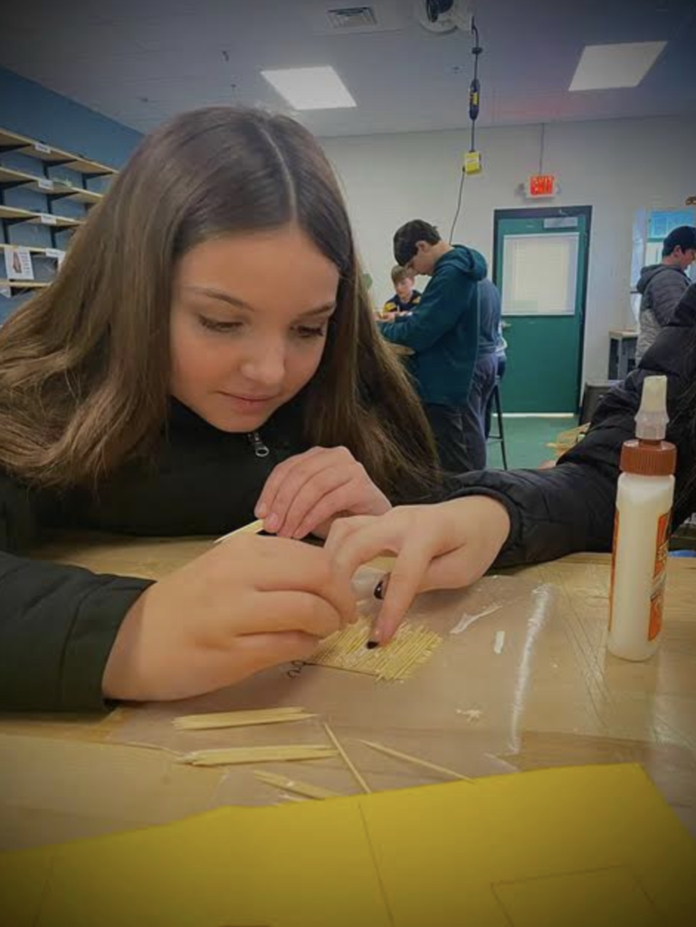 Close-up of a student carefully aligning toothpicks to build a bridge base structure.