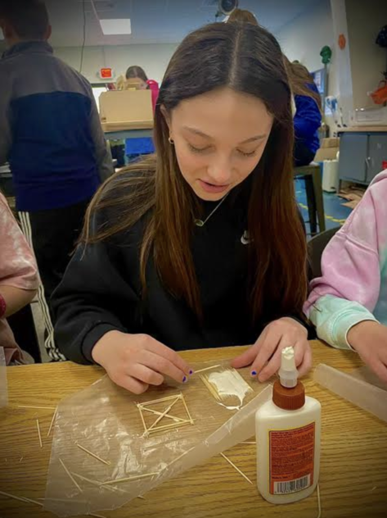 Close-up of a student carefully aligning toothpicks to build a bridge base structure.