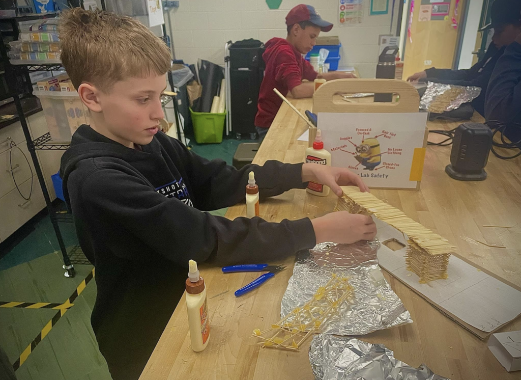 Student works at a lab table carefully gluing toothpicks together while building a bridge structure.