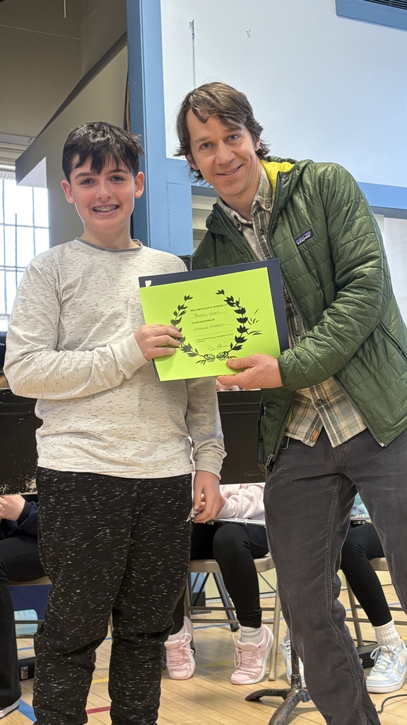 Student and adult pose together in the gym while holding a green certificate, celebrating the student’s achievement.
