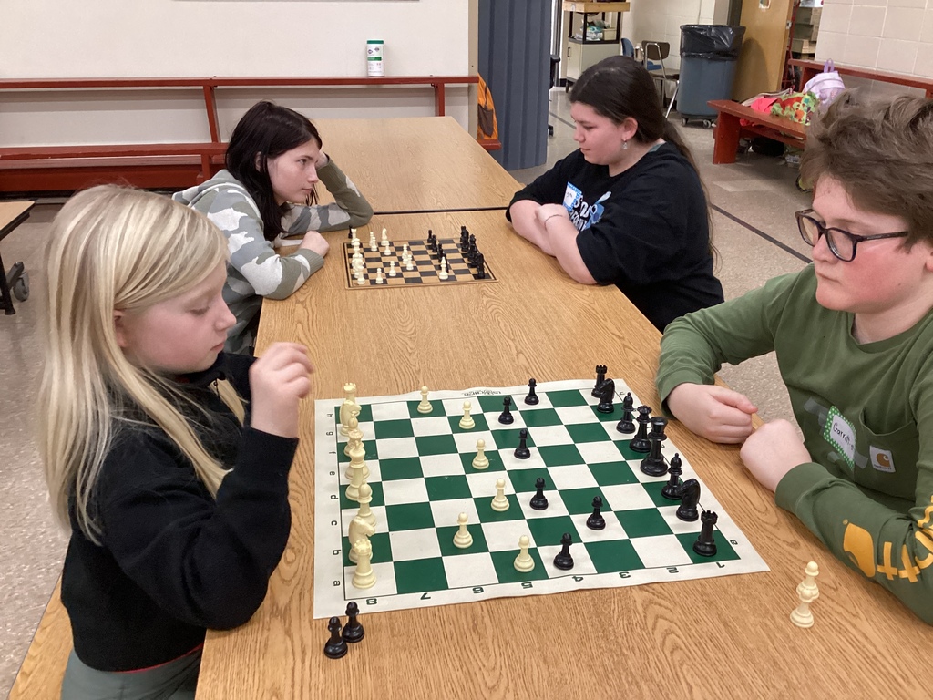 Two students study a chessboard closely while playing a match during a busy chess exhibition in the school cafeteria.