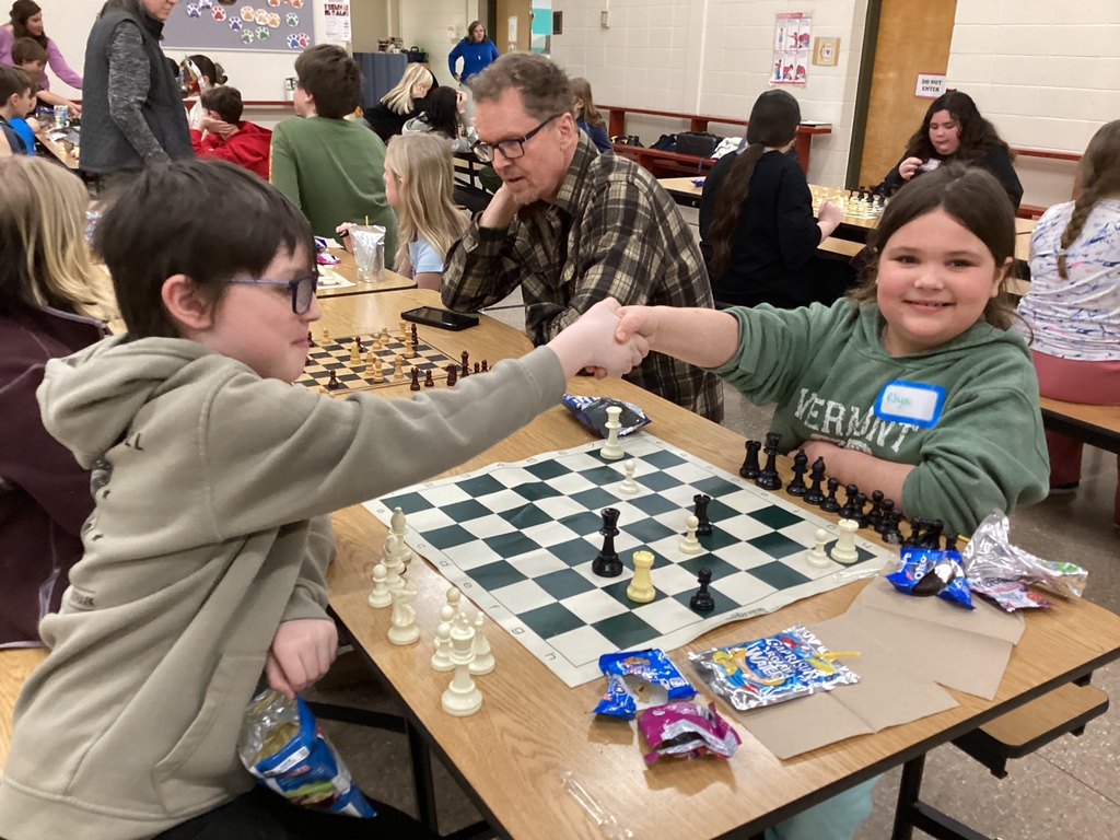 Two students shake hands across a chessboard after finishing a game while other students play chess at tables in the Castleton Elementary cafeteria.