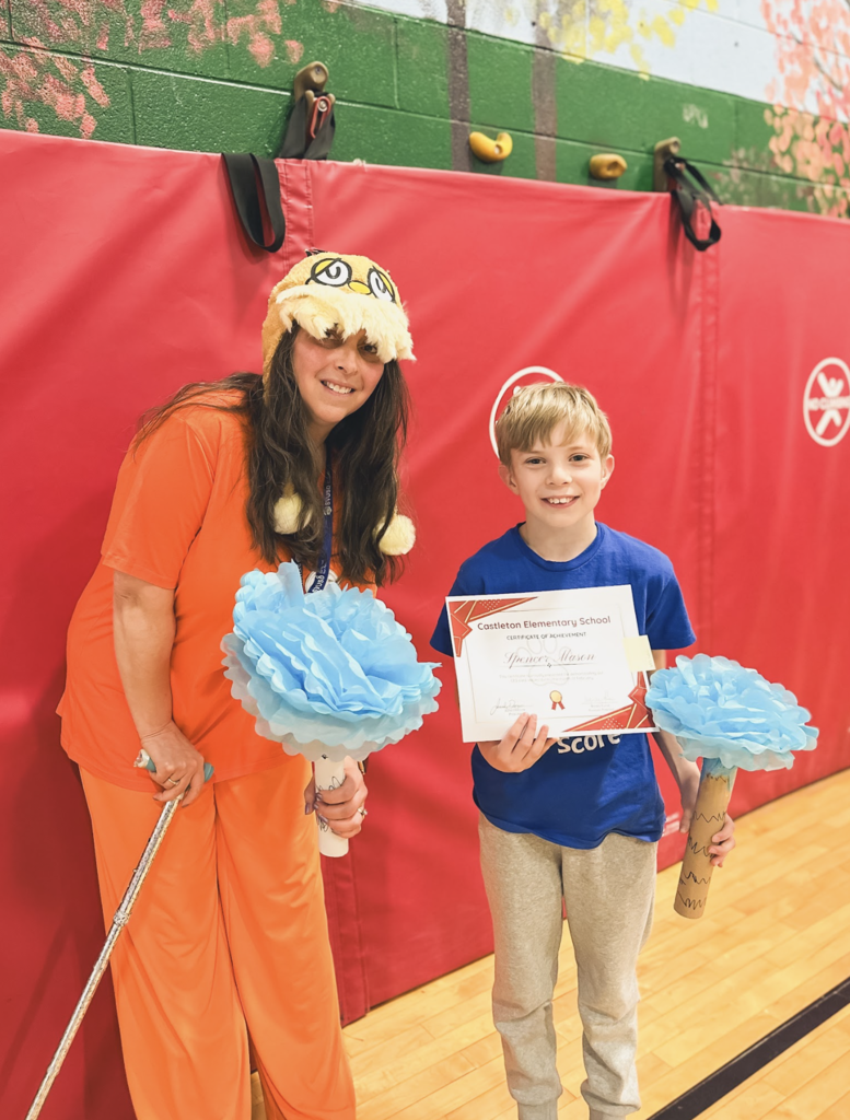 A staff member dressed in a colorful costume stands beside a student holding a Castleton Elementary School certificate of achievement.