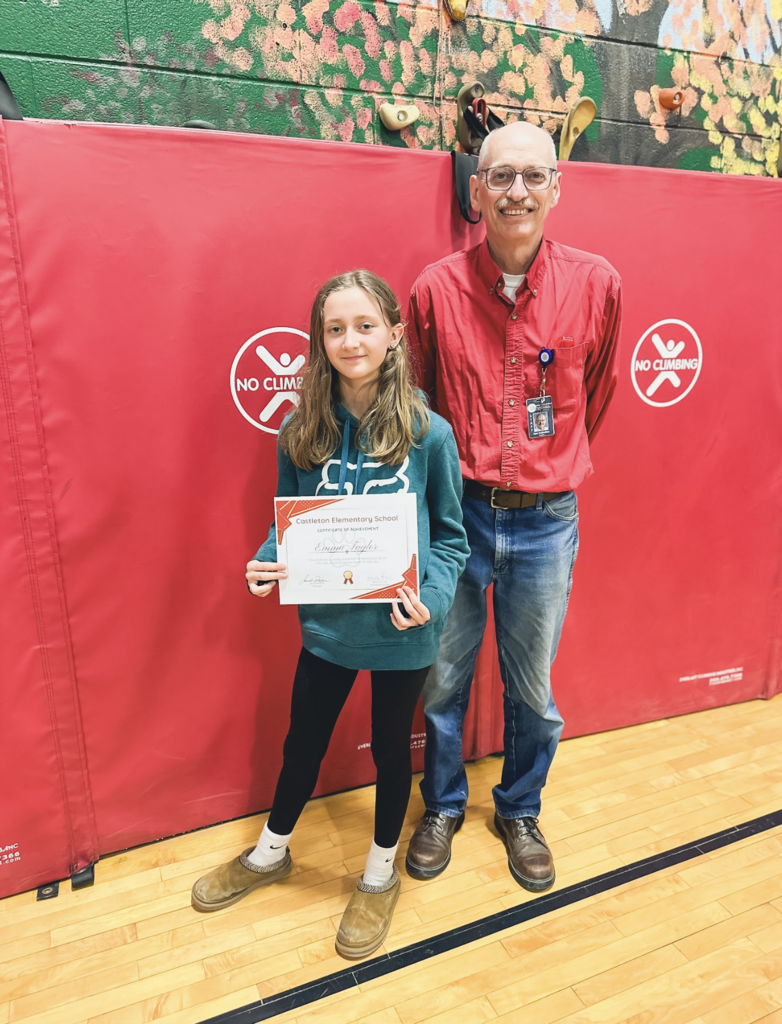 Student holding a Castleton Elementary School certificate stands with a staff member wearing a red shirt in the gym.