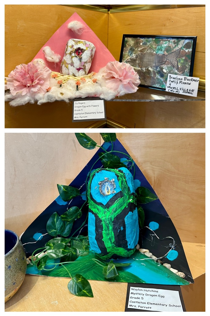 Two student art projects: a pink and white dragon egg on cotton with flowers by Jiy Rogers, and a blue and black dragon egg with green paint and LED lights by Waylon Hutchins.