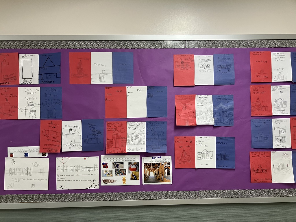 Classroom Bulletin Board Overview A wide shot of a purple bulletin board featuring several student projects about the three branches of U.S. government. Each project consists of three pieces of construction paper—red, white, and blue—taped side-by-side. Below the government projects are math worksheets showing multiplication tables and word problems, along with a few printed photos of toys and a stable.  