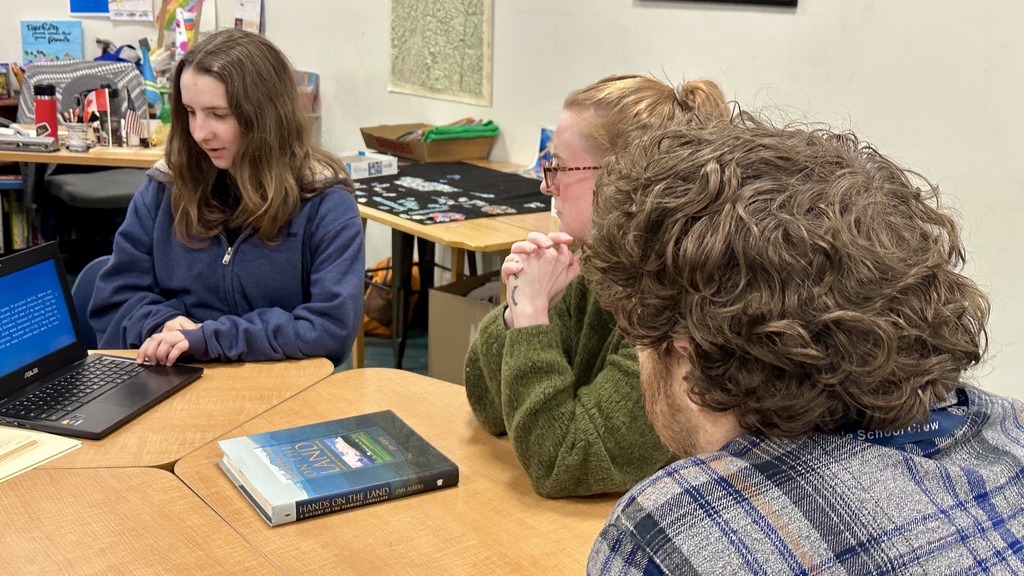 A teacher presents information on a laptop to two colleagues seated at a table during a small-group professional development discussion.