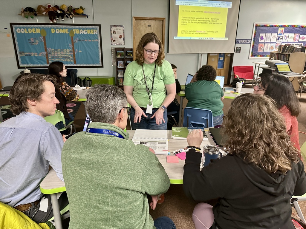 A group of educators sit together at a table reviewing materials and discussing instructional resources during a collaborative professional learning session in a school library.