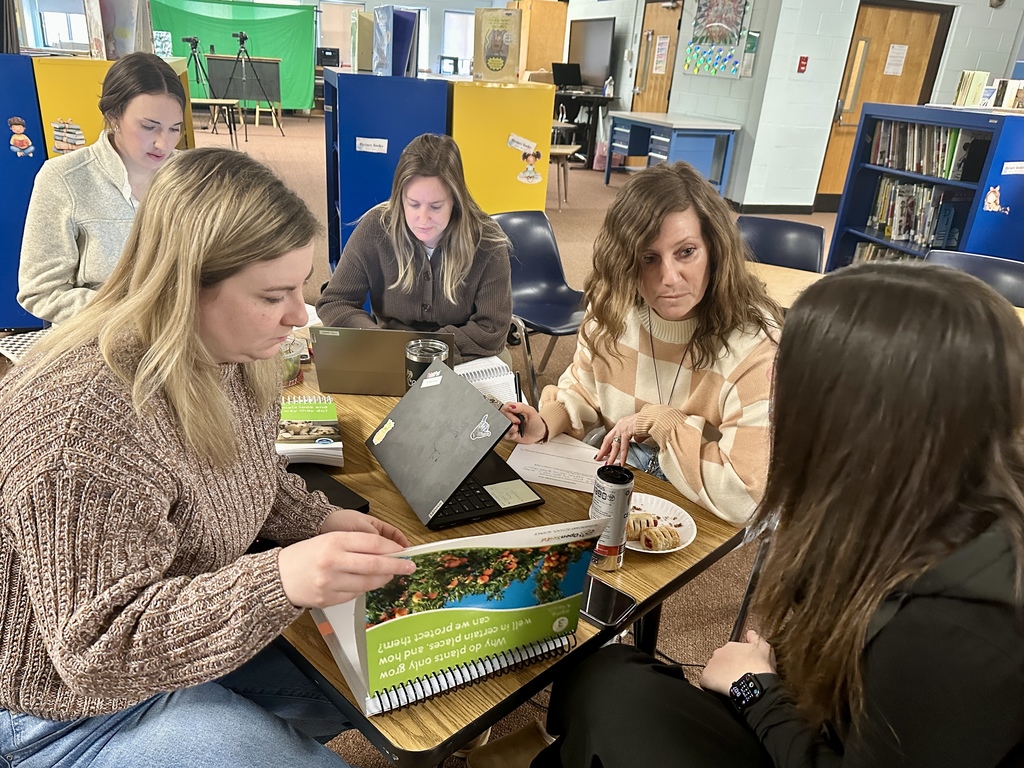 A group of educators sit together at a table reviewing materials and discussing instructional resources during a collaborative professional learning session in a school library.