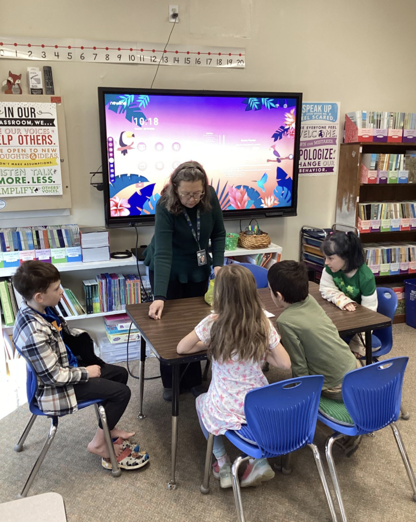 Teacher works with a small group of students seated around a table in a classroom.