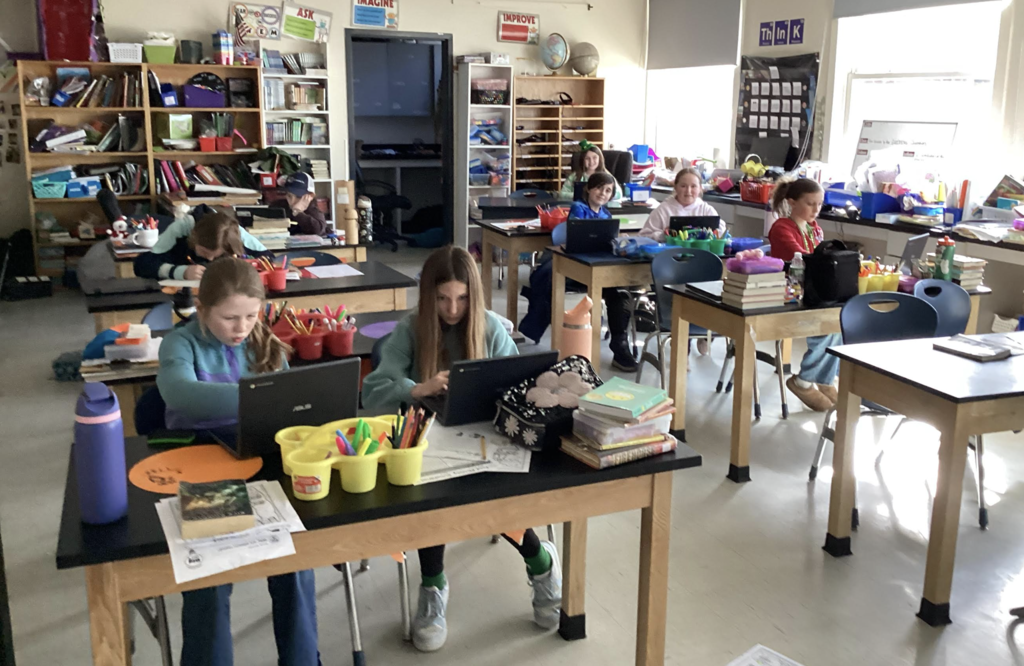 Students sit at lab tables using laptops and working independently in a classroom.