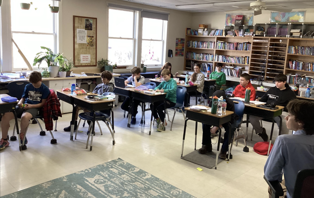 Students sit at desks working quietly on assignments in a classroom.