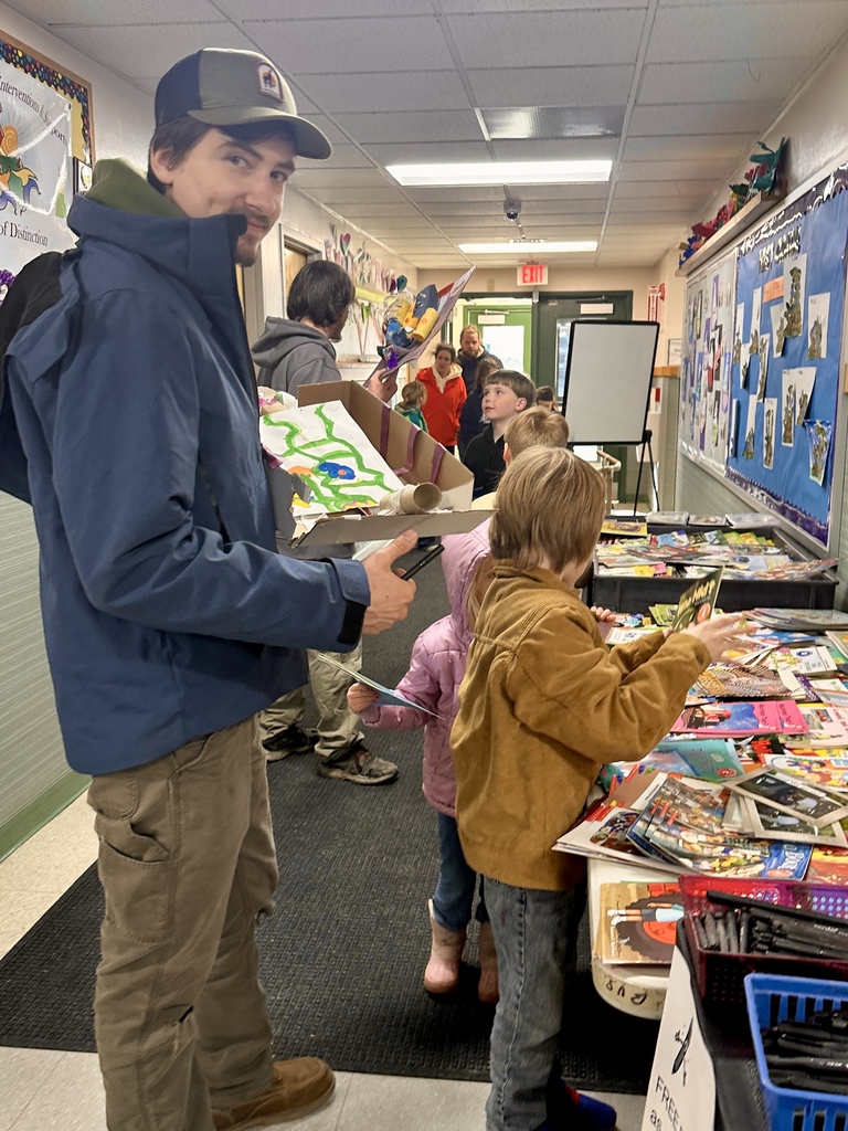 An adult and several children stand in a school hallway looking at student work and materials displayed on a table during the STEAM showcase.