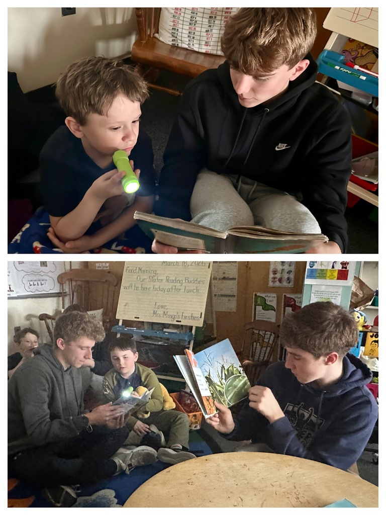 Two students sit on the floor reading together, one using a small flashlight to follow along with the text in a dim reading area.