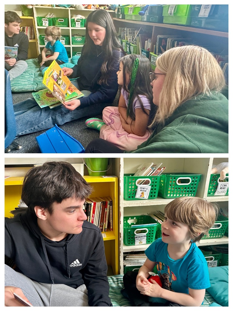 A high school student and a younger student sit together reading a large book titled “Rescue Boat” in a classroom setting.