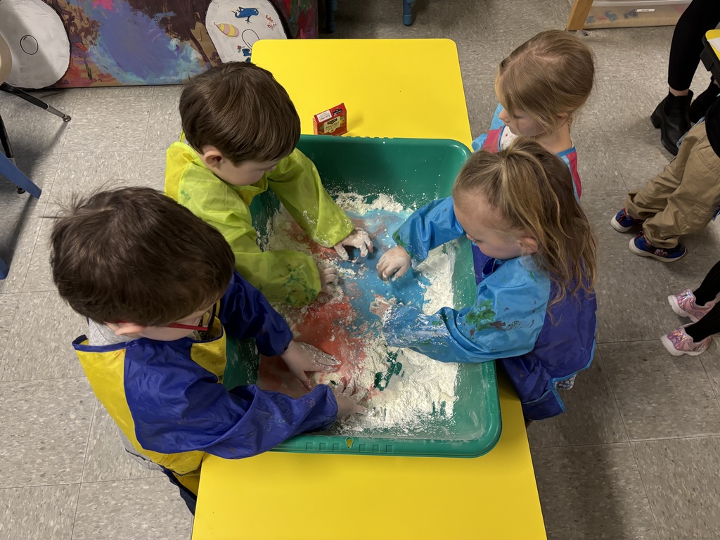 Preschool students reach into a sensory bin filled with oobleck, stretching and squeezing the mixture as part of a hands-on activity.