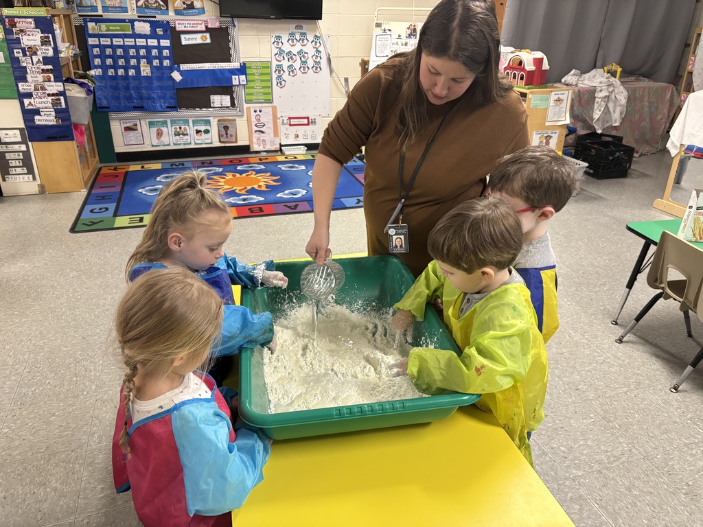 A teacher pours liquid into a green sensory bin as preschool students mix the oobleck, creating a messy, hands-on science activity.
