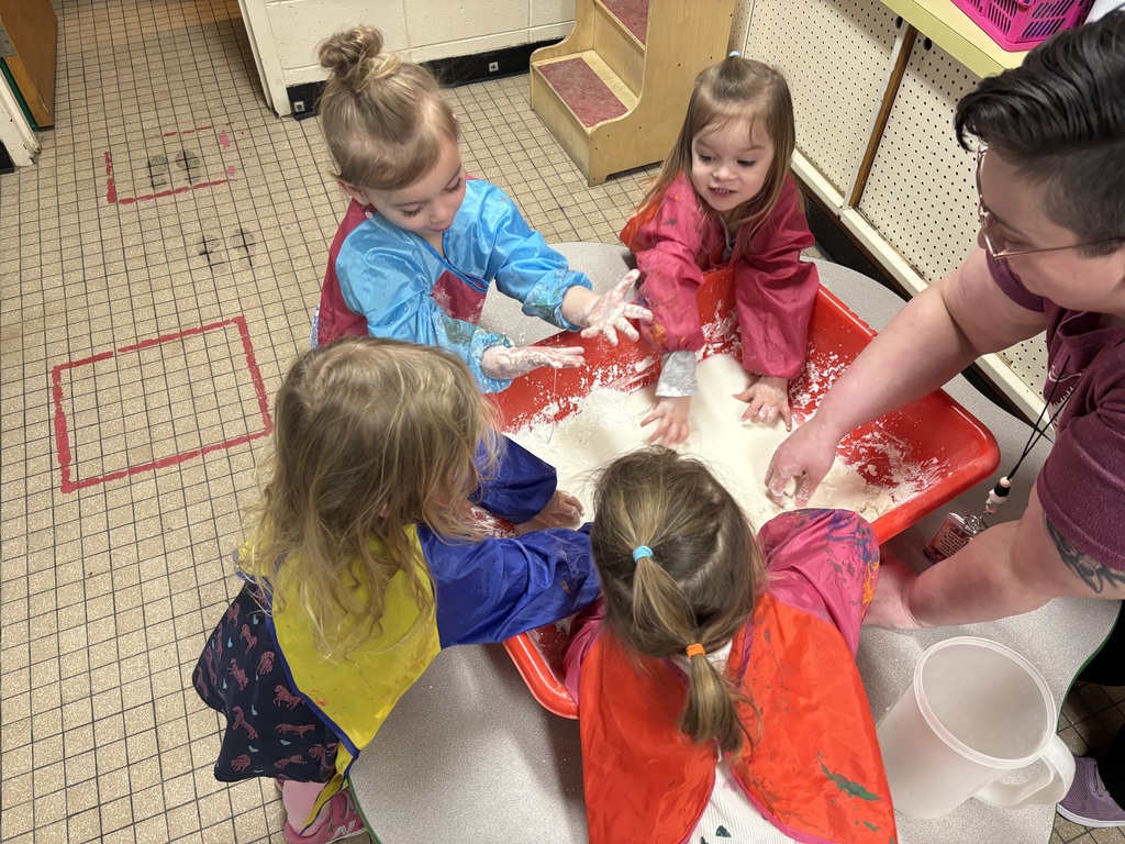 A close-up view of preschool students’ hands mixing oobleck in a sensory bin, showing the messy texture of the activity.