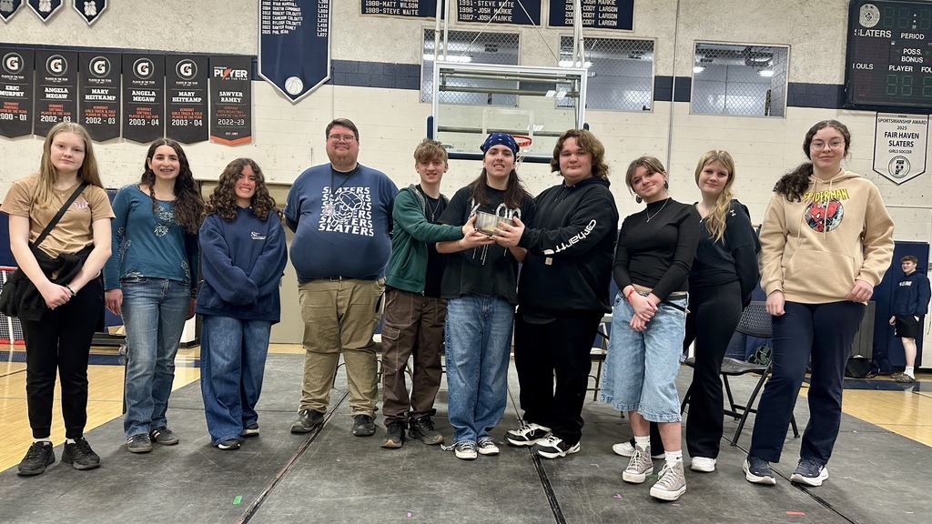 A group of students stands together on a stage in a gymnasium posing with a pot prop after a performance.