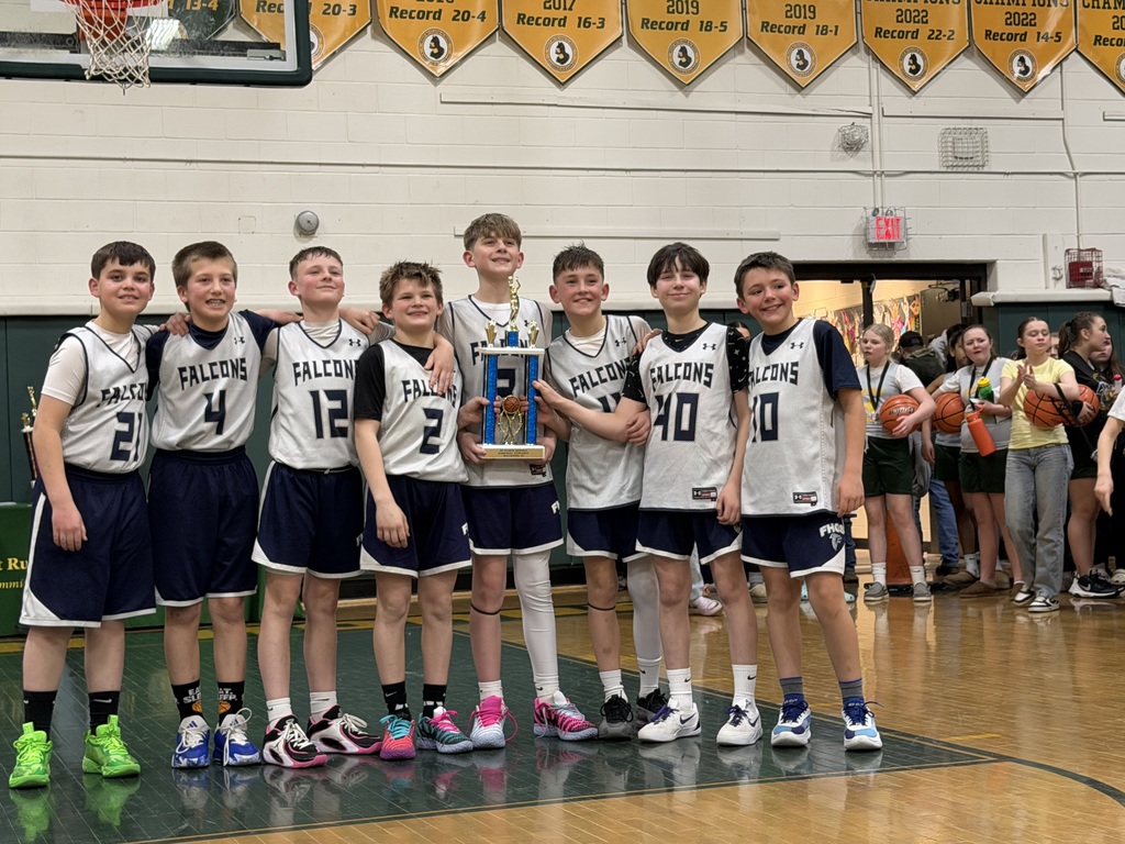 A youth basketball team in matching Falcons uniforms stands together on a gym court holding a trophy, smiling after their tournament finish.