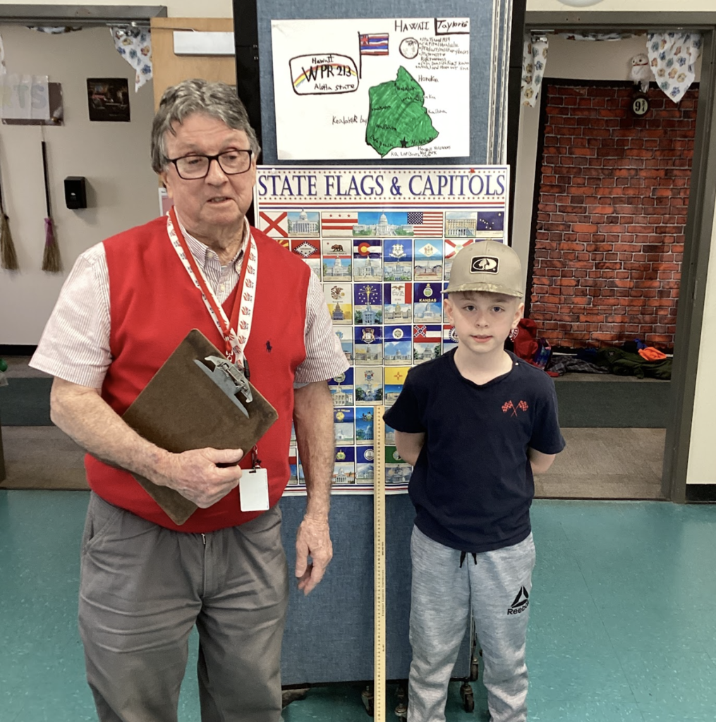 Teacher and student pose in front of a state display board, with a Hawaii project poster above.