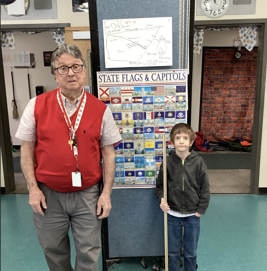 Teacher and student pose beside a state display board, with a hand-drawn Arkansas project poster above.