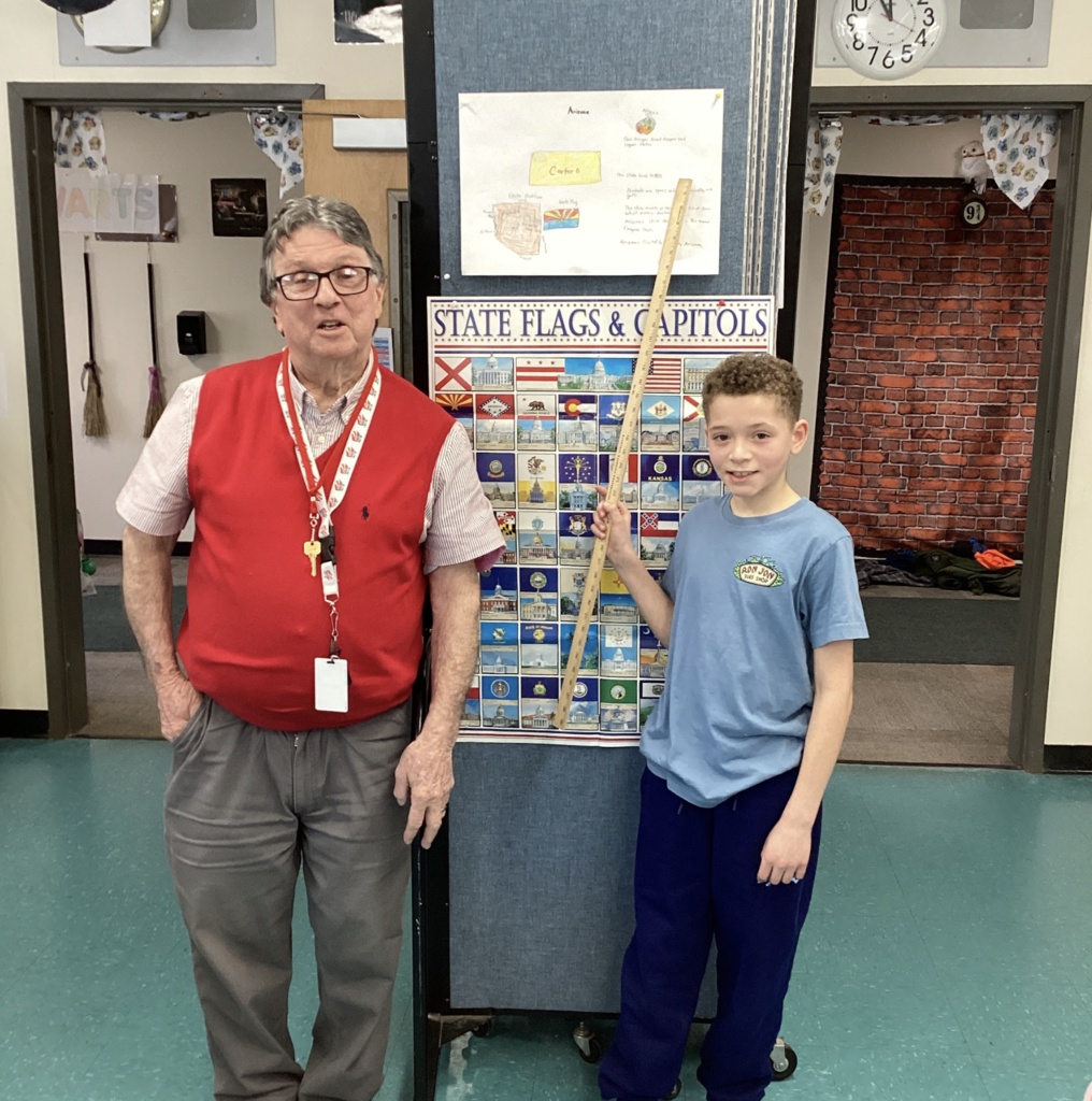 Teacher stands next to a student holding a yardstick, with a state display board and an Arizona project visible above.