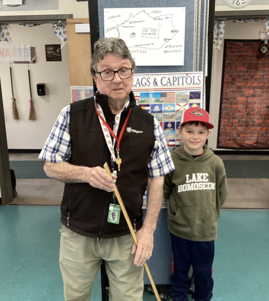 Teacher and student stand with a yardstick in front of a Wisconsin project and state display board.