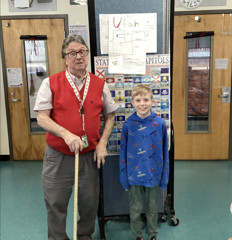 Teacher and student stand beside a “State Flags & Capitals” board with a Utah project displayed above.