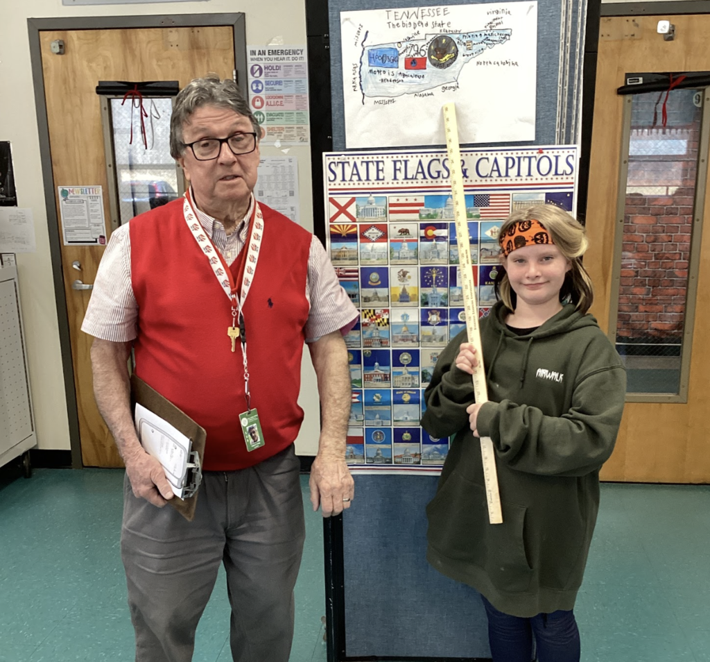 Teacher and student pose with a yardstick in front of a Tennessee project and state display board.