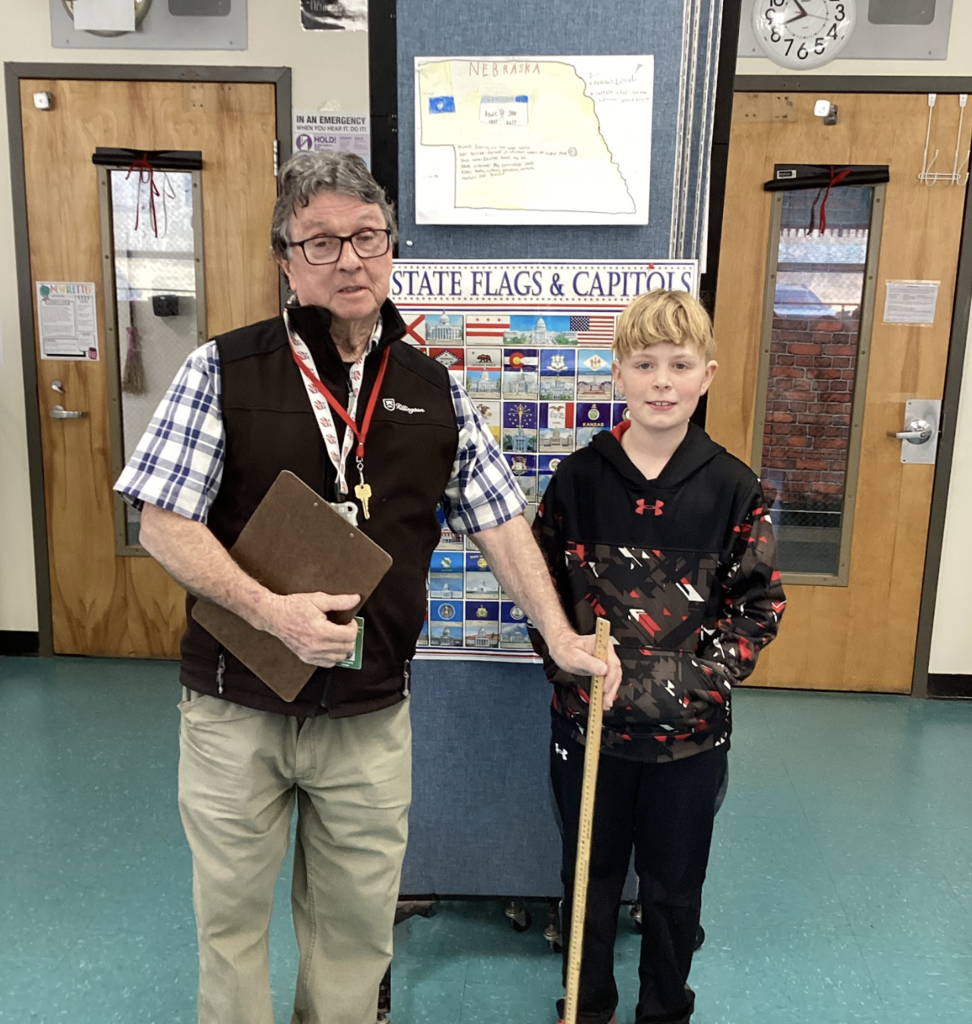 Teacher and student pose with a yardstick in front of a Nebraska project and state display board.