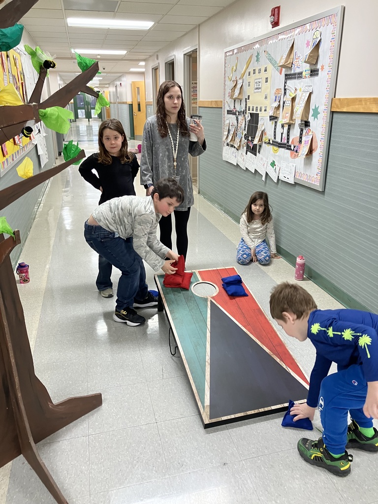 A group of elementary school children playing cornhole in a school hallway. 