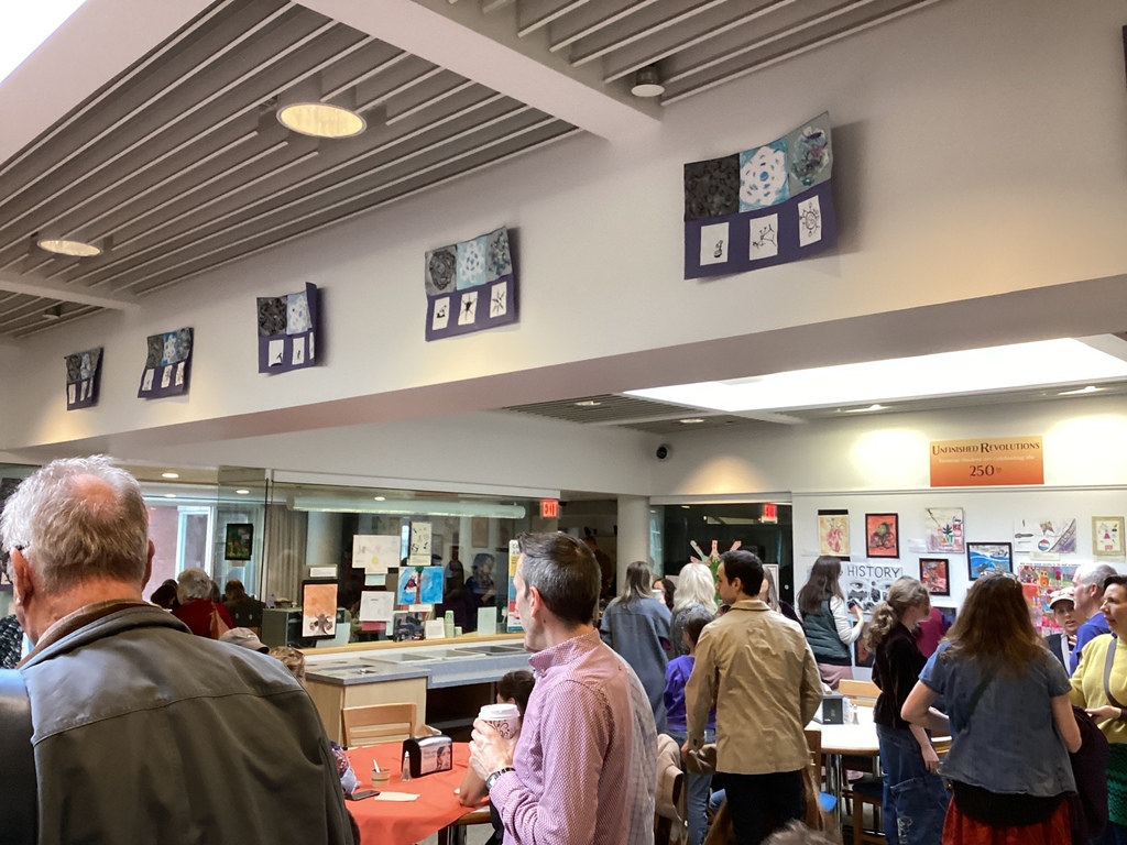 People gather in a reception area with artwork on display, while children and adults explore exhibits together.