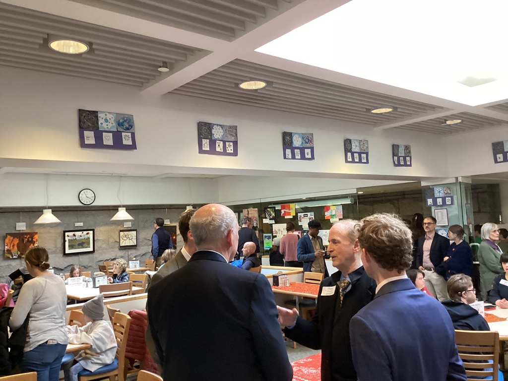 Visitors mingle and view artwork exhibits displayed along a wall inside a public building.