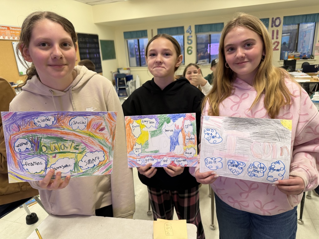 Three students stand together holding posters filled with encouraging words and colorful designs, created to support older students during testing.