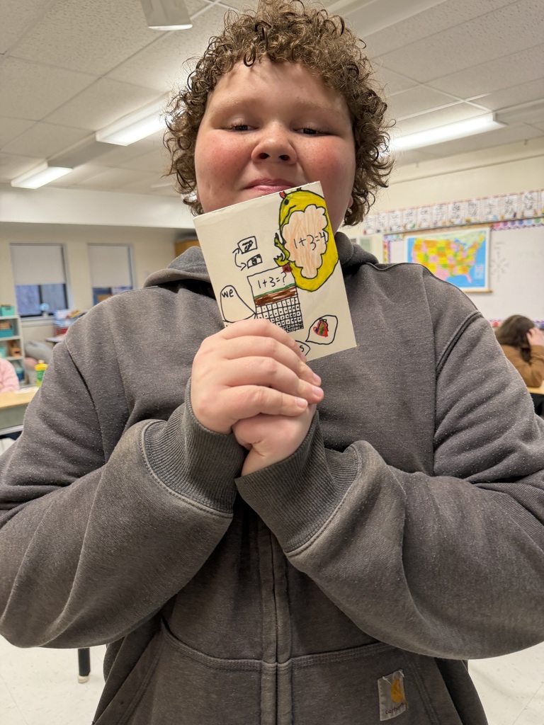A student stands in a classroom holding a small illustrated card with drawings and numbers, part of a set of encouraging messages created for older students.