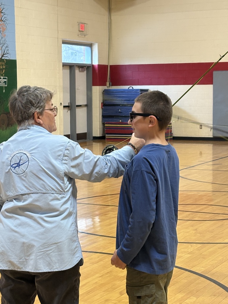 Instructor gives one-on-one guidance to a student wearing sunglasses while demonstrating fly fishing technique in a gym.