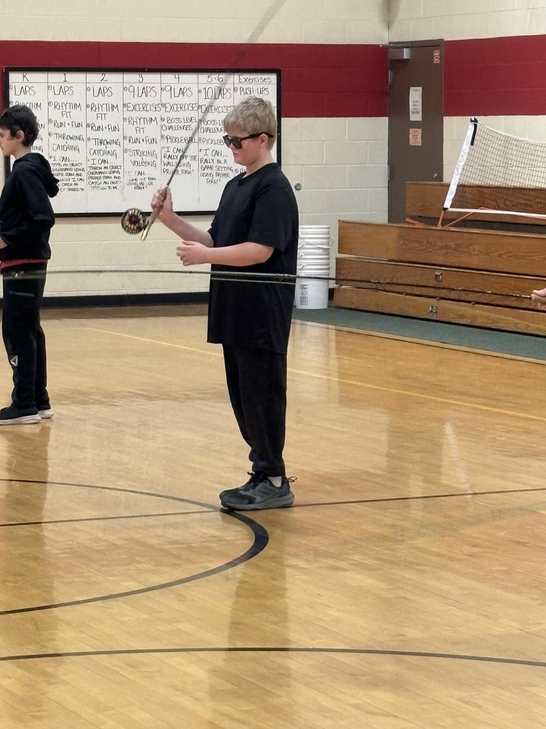 Student practices fly fishing casting alone in a gym, holding a rod and focusing on technique.